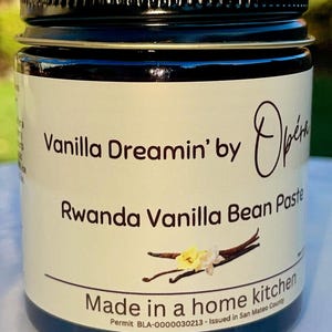 May include: A glass jar with a black lid containing Rwanda Vanilla Bean Paste, labeled "Vanilla Dreamin' by Opéra" and "Made in a home kitchen. Permit BLA-0000030213 - Issued in San Mateo County."