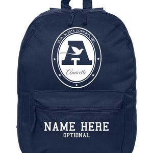 May include: Navy blue backpack with a front pocket and a top handle. The backpack features a white oval emblem with the text "Zeta Phi Beta Sorority, Inc." and a stylized "A" with a dove. Below the emblem is the word "Amicelle". The front pocket has the text "NAME HERE OPTIONAL".