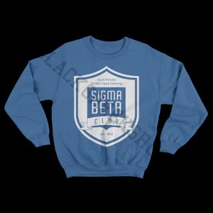 以下が含まれることがあります： 白い紋章がついた青いスウェットシャツ。紋章には「South Affiliate Phi Beta Sigma Fraternity」、「Sigma Beta Club」、「est. 1950」の文字が書かれている。