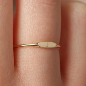 May include: A gold ring with a flat, rectangular band and the letter "J" engraved on the top.
