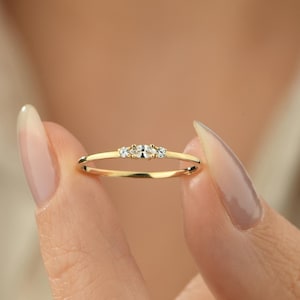 May include: A delicate gold band ring with three small, clear gemstones set in a row.