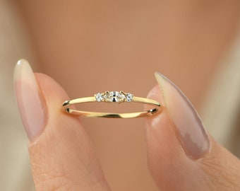 May include: A delicate gold band ring with three small, clear gemstones set in a row.