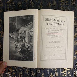 May include: An open book with the title "Bible Readings for the Home Circle" and an illustration on the left page. The book is a "New, Revised, and Enlarged Edition" with over 300 illustrations.