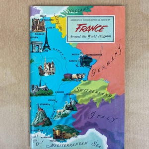 May include: A vintage illustrated map of France with the title "France Around the World Program" and the text "American Geographical Society". The map shows major cities and geographical features of France, including Paris, Lyon, Marseille, and the Mediterranean Sea.