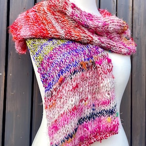 Könnte beinhalten: Ein mehrfarbiger, handgestrickter Schal, präsentiert auf einer Schaufensterpuppe. Der Schal hat eine Mischung aus Rosa, Rot, Lila und Gelb. Die Textur ist dick und gemütlich, ideal, um jedem Outfit einen Farbtupfer zu verleihen. Ein einzigartiges, handgefertigtes Accessoire.