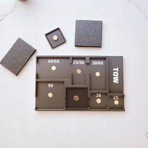 May include: A dark gray, multi-compartment organizer with magnetic closures and the word "TOW" printed on the side. The organizer has various labeled sections with numbers and magnetic dots. Three separate gray textured squares are also present.