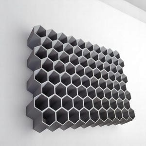 May include: A grey, honeycomb-shaped wall decoration. The geometric design features numerous hexagonal cells, creating a three-dimensional effect. It is mounted on a white wall, showcasing its modern aesthetic.