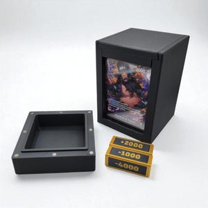 Könnte beinhalten: Schwarzer Karten-Display-Kasten mit klarer Front, der eine farbenfrohe Sammelkarte zeigt. Daneben befinden sich schwarz-goldene Token mit den Werten +2000, -1000 und -4000. Eine separate schwarze Ablage ist ebenfalls vorhanden.