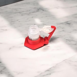 May include: A red plastic bottle holder with a clear bottle inside. The bottle has a label that says "Safe Colour".