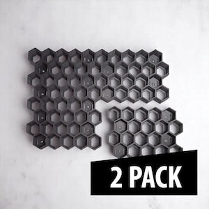 May include: Dark gray honeycomb-shaped molds, perfect for creating unique designs. The molds are arranged in three sections, with the text "2 PACK" in a black rectangle in the lower right corner. The molds are made of a durable material.