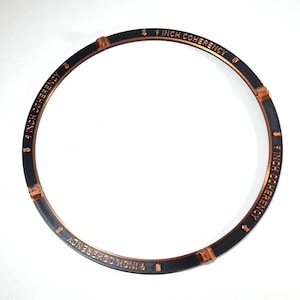 May include: A circular black ring with copper-colored accents and text. The text 9 INCH COHERENCY is printed in copper lettering along the circumference, interspersed with small copper arrow symbols and three distinct copper-colored connector joints.