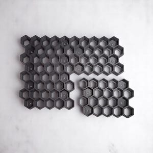 May include: A set of two gray plastic honeycomb-shaped molds. The molds are made up of hexagonal shapes and are designed for creating decorative items.