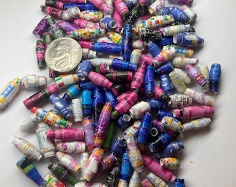 May include: A large pile of colorful paper beads in various patterns and colors, including blue, pink, purple, and white. The beads are made from rolled up paper and have a slightly textured surface.