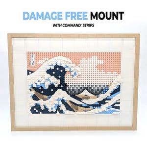 May include: A rectangular wall art piece constructed from interlocking plastic building bricks, depicting a stylized ocean wave in shades of blue, white, and tan. The text DAMAGE FREE MOUNT WITH COMMAND STRIPS is printed above the framed artwork.