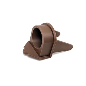 May include: A brown plastic 3D printed object with a round hole in the center and two pointed legs. The object is designed to hold a small item, such as a pen or pencil.