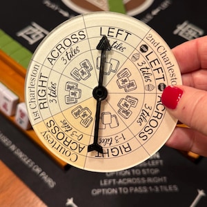 May include: A circular Mahjong game direction indicator with a black arrow. The indicator has text that says "LEFT", "RIGHT", and "ACROSS". The indicator is held over a black game board with Chinese characters.