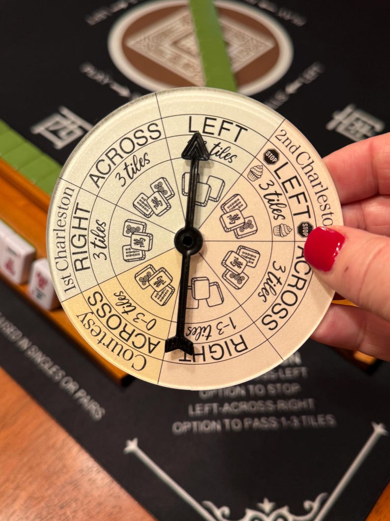 May include: A circular Mahjong game direction indicator with a black arrow. The indicator has text that says "LEFT", "RIGHT", and "ACROSS". The indicator is held over a black game board with Chinese characters.