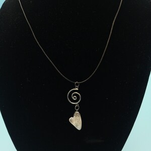 May include: A silver necklace with a heart-shaped pendant and a spiral charm. The necklace is on a black display stand.