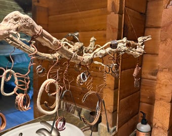 Puede incluir: Una rama de madera flotante suspendida por hilos finos, que sirve como expositor para varios anillos y pulseras. Las piezas de joyería están hechas de alambre de cobre, metal trenzado y bandas texturizadas, colgadas de ganchos de alambre.