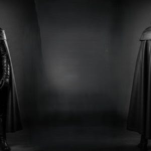 May include: A black leather costume with a hooded cloak. The costume includes a full-face mask, a tunic with a belt, gloves, and boots. The image shows the costume from the front and back, set against a dark gray background.