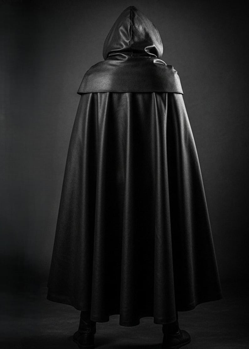 May include: A black hooded cloak, viewed from the back, with a smooth, leather-like texture. The cloak has a wide, flowing design, and the hood is up. The image is set against a dark background, emphasizing the garment's silhouette.