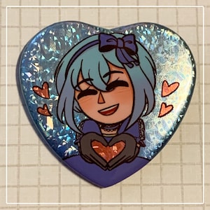 Puede incluir: Botón en forma de corazón con una ilustración de dibujos animados de un personaje sonriente con cabello azul y un lazo. El personaje sostiene un corazón y está rodeado de corazones flotantes. El fondo tiene un efecto iridiscente y brillante.