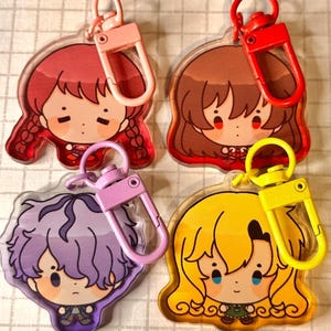 以下が含まれることがあります： 漫画のキャラクターデザインが施されたアクリルキーホルダー4個セット。各キーホルダーは、赤、茶色、紫、黄色の異なる髪の色をしています。キーホルダーには、ピンク、赤、ピンク、黄色の色付きクラスプが付いています。キャラクターはかわいい表情をしています。