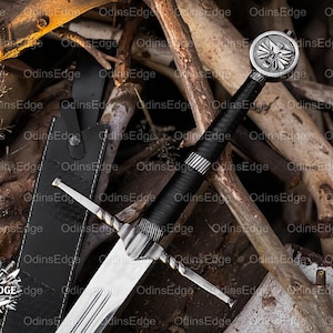 May include: A silver and black sword with a leather-wrapped handle and a crossguard. The sword has a double-edged blade and a circular pommel with a wolf emblem. A black leather sheath is visible.