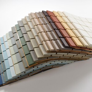 May include: A selection of small, rectangular ceramic tiles in various colours, including blue, green, grey, brown, and white. The tiles are arranged in a layered fan shape, demonstrating the different colour options for home decor projects.