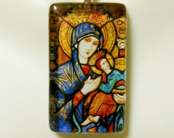 Puede incluir: Un collar de cadena de plata con un colgante rectangular de vidrio que presenta una imagen de vitral de la Virgen María sosteniendo a un bebé Jesús. La imagen está sobre un fondo dorado con un halo alrededor de la cabeza de la Virgen María.