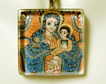 Puede incluir: Un collar de cadena de plata con un colgante cuadrado de vidrio que presenta una imagen colorida de María y Jesús. La imagen es de estilo tradicional con detalles intrincados y colores vibrantes.