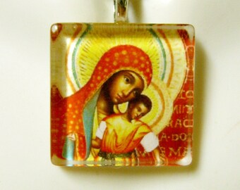 Puede incluir: Un collar de cadena de plata con un colgante cuadrado de vidrio que presenta un icono religioso de una mujer sosteniendo a un niño. El icono es de estilo tradicional con colores rojo, amarillo y azul. El colgante tiene texto alrededor del borde en color rojo oscuro.