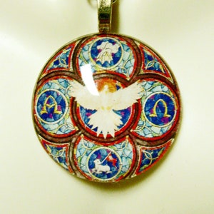 May include: A round glass pendant necklace with a silver chain. The pendant features a stained glass design with a white dove, red, blue and gold accents. The design includes the Greek letters Alpha and Omega.