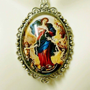 May include: Silver oval pendant necklace with a glass cameo featuring a depiction of the Virgin Mary, known as Our Lady of the Knots, holding a rope in her hands. The cameo is surrounded by a decorative silver frame.
