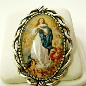 Pode incluir: Um pingente oval de prata com um camafeu de vidro que apresenta uma imagem religiosa da Virgem Maria com uma túnica azul. O pingente tem um design ornamentado detalhado.