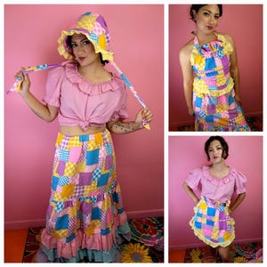 May include: A patchwork skirt, top, and bonnet set in a variety of colors including pink, yellow, blue, and purple. The skirt has a tiered ruffle design. The top is a light pink color with a ruffled neckline. The bonnet has a matching patchwork design.