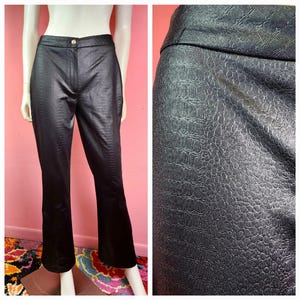 May include: Black faux leather trousers with a textured, crocodile-like pattern. The trousers have a button closure and a slight flare at the bottom. The trousers are displayed on a mannequin.