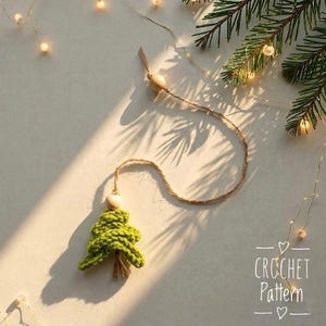 Pode incluir: Enfeite de árvore de Natal de crochê verde feito à mão com uma conta de madeira e barbante. O enfeite é exibido em um fundo claro com luzes de fadas e um galho de sempre-viva. O texto "CROCHET Pattern" é visível.