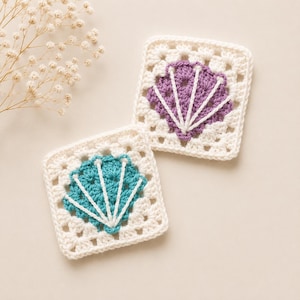 May include: Two square crochet coasters featuring a white border and a central shell motif. One coaster has a purple shell design with white embroidered lines, while the other has a teal shell design with white embroidered lines.