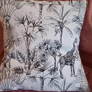 May include: A white throw pillow with a black and white print of tropical plants and a giraffe. The print is a stylized line drawing.