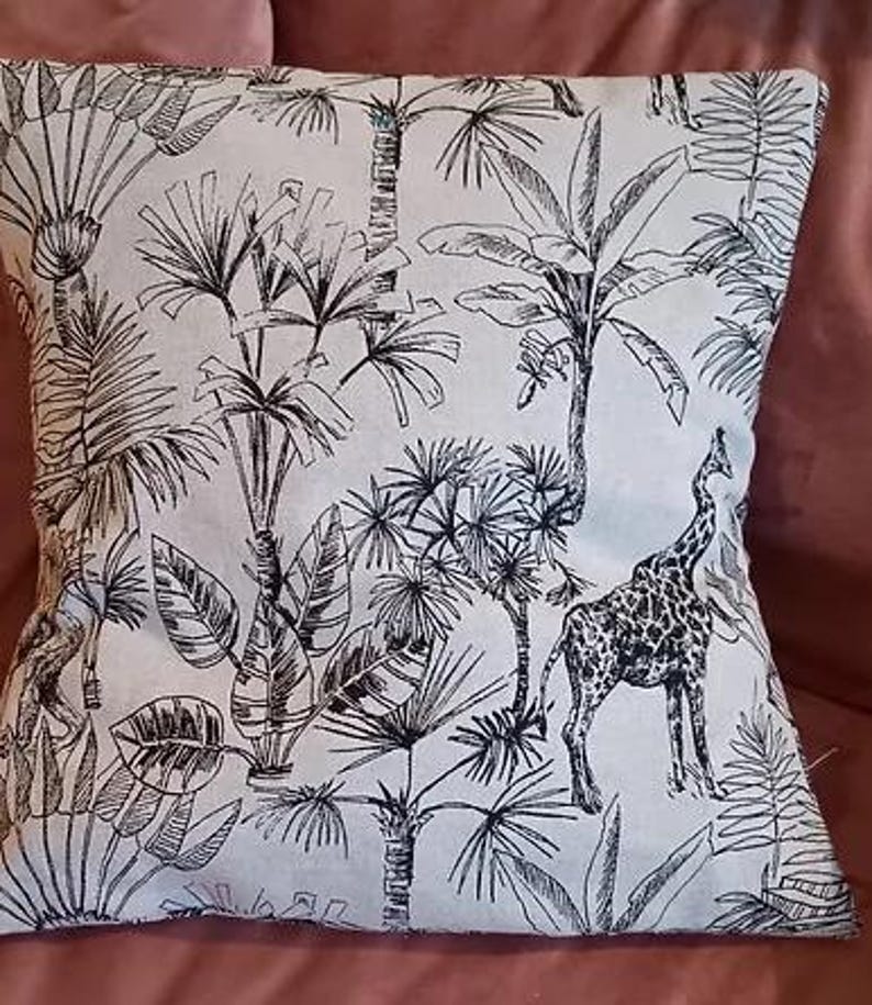 May include: A white throw pillow with a black and white print of tropical plants and a giraffe. The print is a stylized line drawing.