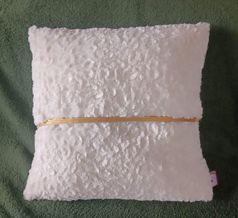May include: White faux fur pillow with a gold zipper detail. The pillow is soft and fluffy.