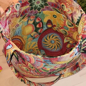 May include: A colorful tapestry tote bag with a floral and geometric design. The bag has a long strap and is made of a thick, woven fabric.