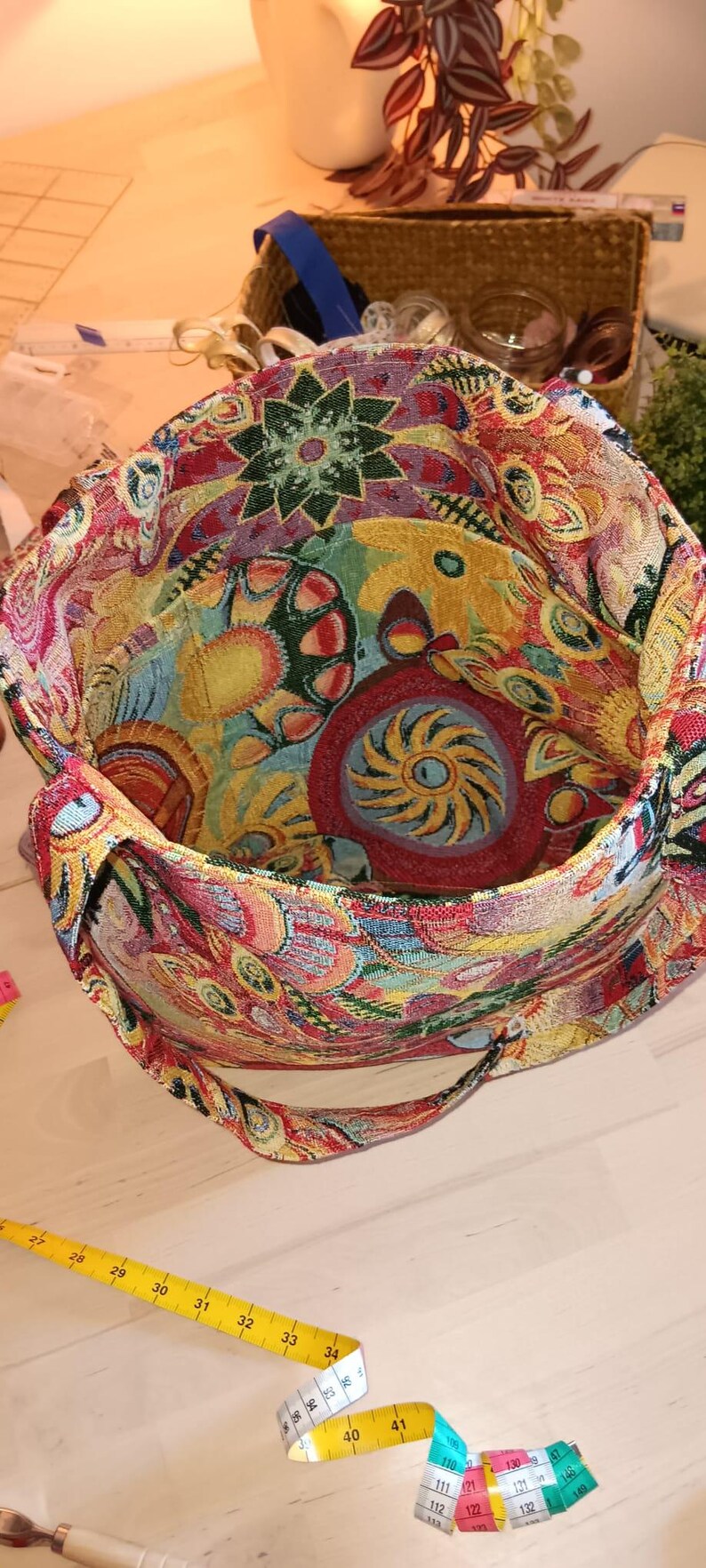 May include: A colorful tapestry tote bag with a floral and geometric design. The bag has a long strap and is made of a thick, woven fabric.