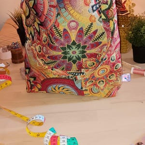 May include: A colorful tapestry bag with a floral design. The bag is sitting on a wooden table with a measuring tape and scissors.