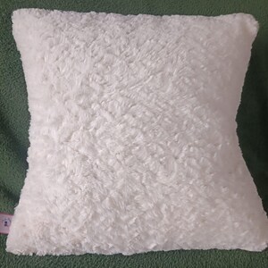 May include: A white fluffy pillow with a soft, plush texture. The pillow is square shaped and has a subtle sheen.