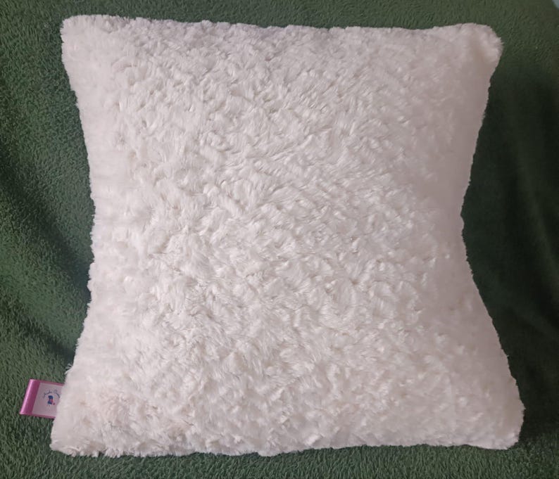 May include: A white fluffy pillow with a soft, plush texture. The pillow is square shaped and has a subtle sheen.