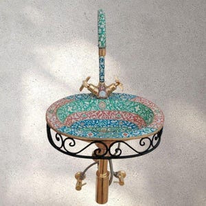 May include: A decorative, circular sink featuring a patterned basin in green, red, and blue. The tap and base are gold-toned, and the sink is supported by a black, wrought-iron stand. The tap has two handles.