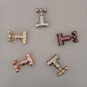 May include: Five miniature metal faucet replicas in various finishes: silver, gold, and copper. Each faucet features a T-shaped body and a three-knob handle. The faucets are arranged on a neutral background.