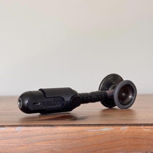 May include: A black stethoscope with a digital recording device attached to the end of the tubing. The stethoscope has a black rubber earpiece and a black metal chest piece.